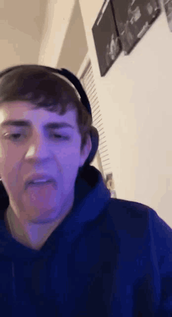 a young man wearing headphones and a blue hoodie is making a face .