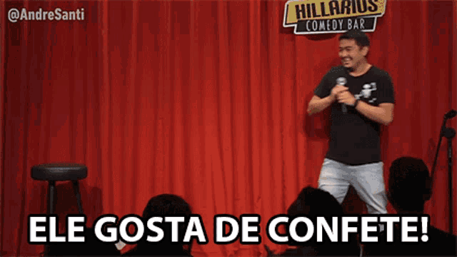 a man stands on a stage holding a microphone with the words ele gosta de confete below him