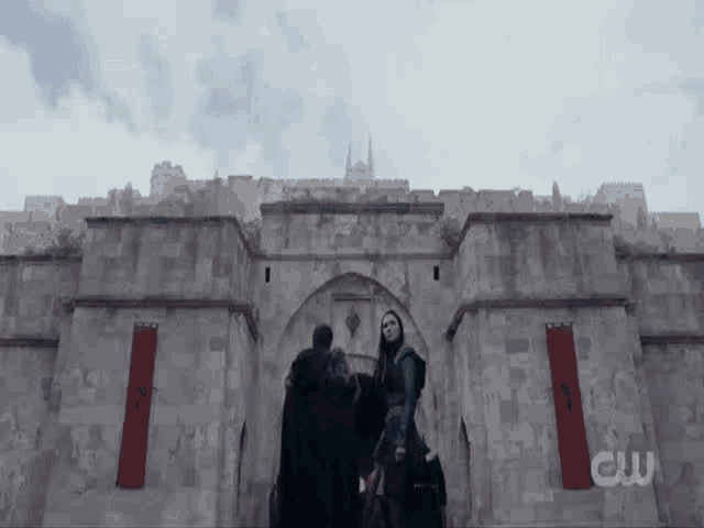 a man and a woman are standing in front of a stone wall .