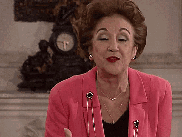 an elderly woman in a pink jacket is standing in front of a clock .