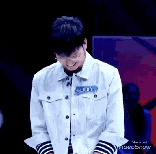 a young man wearing a white jacket and striped sleeves is standing on a stage and smiling .