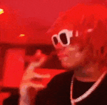 a close up of a person wearing sunglasses and a necklace in a red room .
