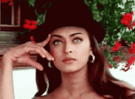 a woman wearing a top hat and hoop earrings looks to the side