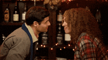 a man and a woman are looking at each other in front of a shelf with bottles of alcohol on it