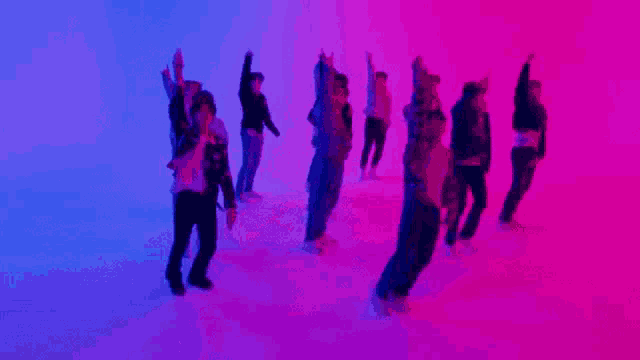 a group of people are dancing in a room with a pink and blue light behind them .