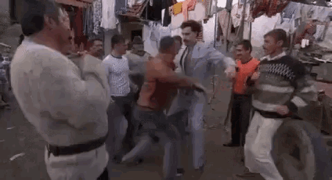 a group of men are standing around a man in a suit dancing on a street .