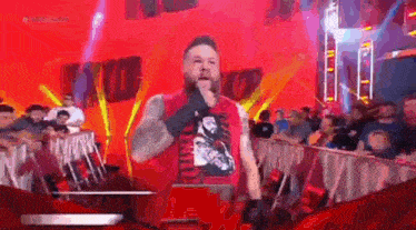 a man in a red shirt is standing on a stage in front of a crowd while talking into a microphone .