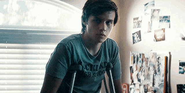 a young man with crutches is standing in front of a window in a room with pictures on the wall .