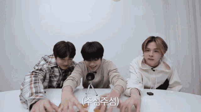 three young men are sitting at a table with their hands outstretched and one of them is wearing a microphone