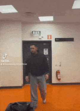a man is walking in a hallway with a fire extinguisher on the wall