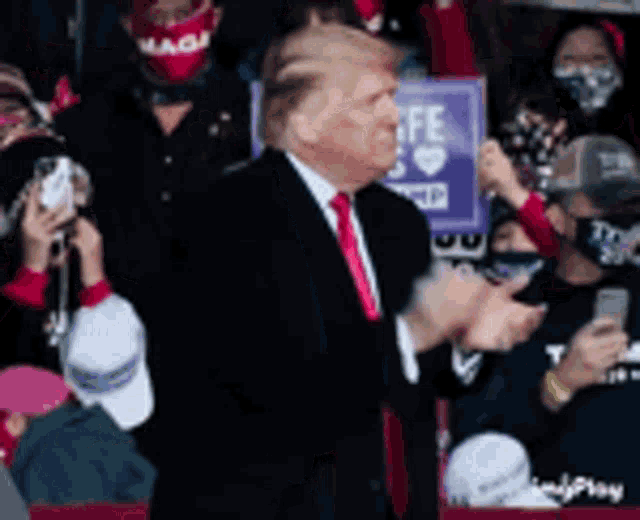a man in a suit and tie is standing in front of a crowd applauding ..