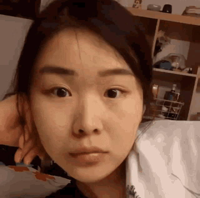a close up of a woman 's face without makeup in front of a shelf .