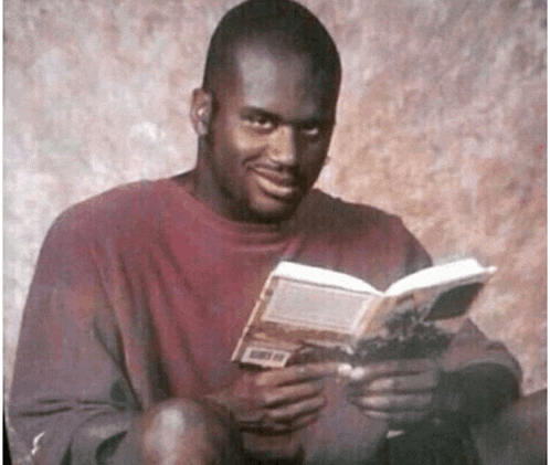 a man in a red shirt is reading a book and smiling at the camera