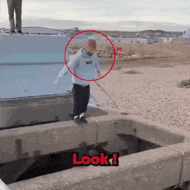 a man in a supreme hoodie is jumping over a hole in a concrete wall