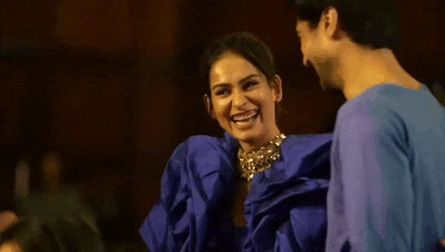 a man and a woman are laughing together while standing next to each other . the woman is wearing a blue dress .