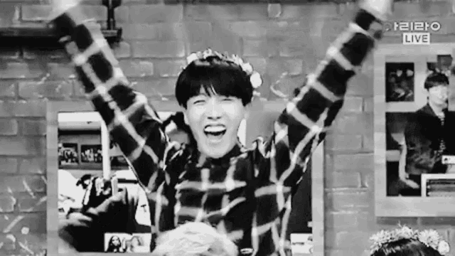 a black and white photo of a boy wearing a flower crown and raising his arms in the air .