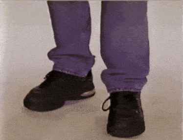 a person wearing purple jeans and black shoes is standing on a white surface