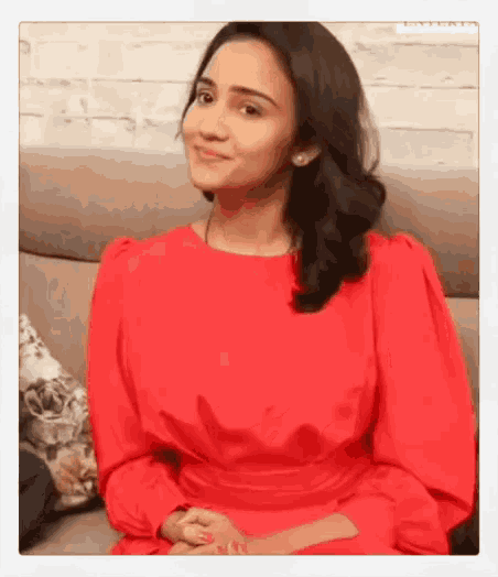 a woman wearing a red dress is sitting on a couch