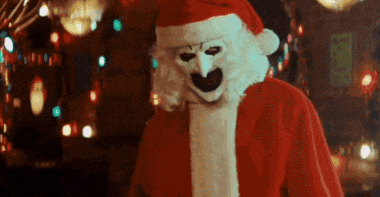 a man in a santa claus costume with a white mask on his face is standing in front of a christmas tree .