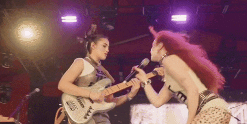 a woman is playing a guitar while another woman sings into a microphone on a stage .