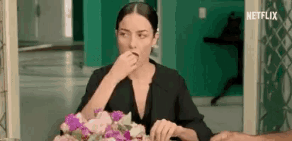 a woman is sitting at a table with a bouquet of flowers and eating a piece of food .