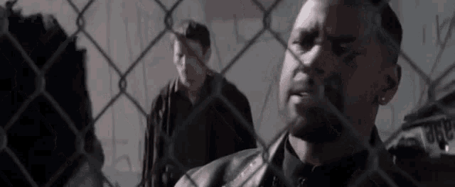 two men are standing behind a chain link fence .