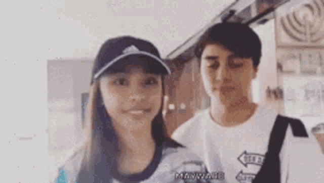 a boy and a girl are standing next to each other and the girl is wearing a hat that says adidas