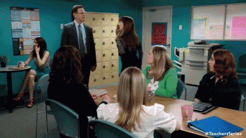 a group of women sit around a table with a man in a suit and tie standing in the background