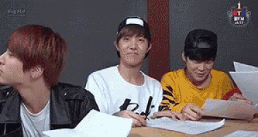a group of young men are sitting at a table with papers and a laptop .