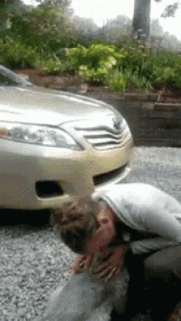 a woman kisses a dog in front of a silver car