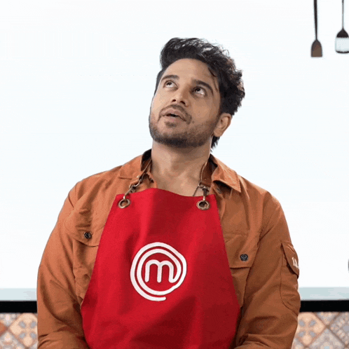a man wearing a red apron with the letter m on it looks up