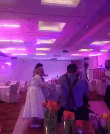 people are dancing in a room with purple lights on the ceiling