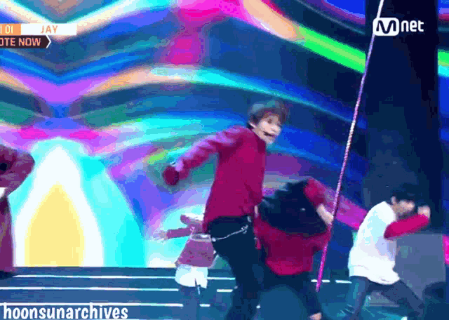 a man in a red shirt is dancing on a stage in front of a mnet banner