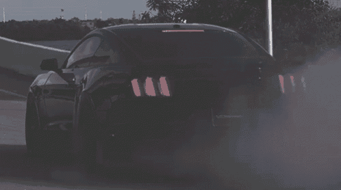 a black car is driving down a road and smoke is coming out of the back