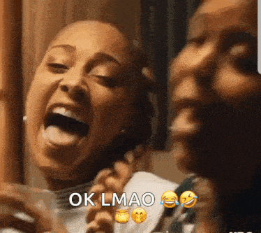 a couple of women are laughing together and one of them is holding a cell phone .