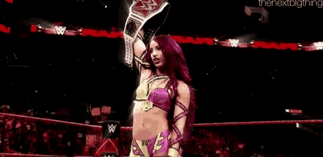a woman with red hair is holding a wrestling championship belt in a wrestling ring .