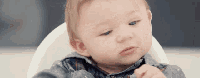 a baby is sitting in a high chair and looking at something .