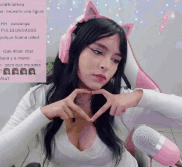a woman making a heart shape with her hands while wearing pink headphones
