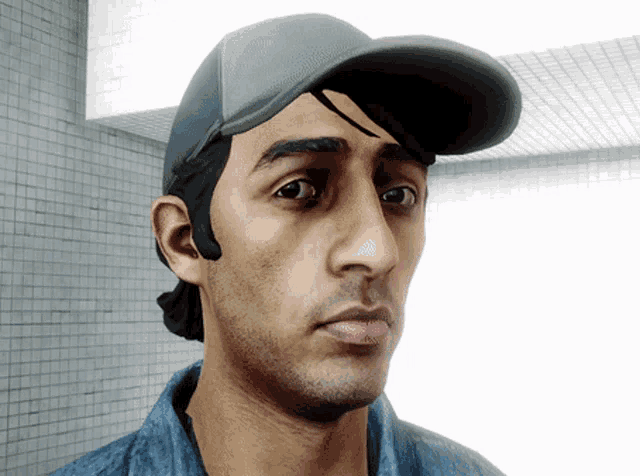 a man wearing a hat and a blue shirt looks at the camera