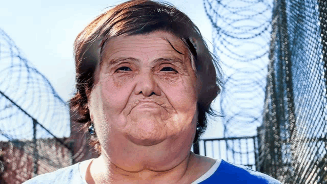 a woman in a blue shirt stands in front of barbed wire fence