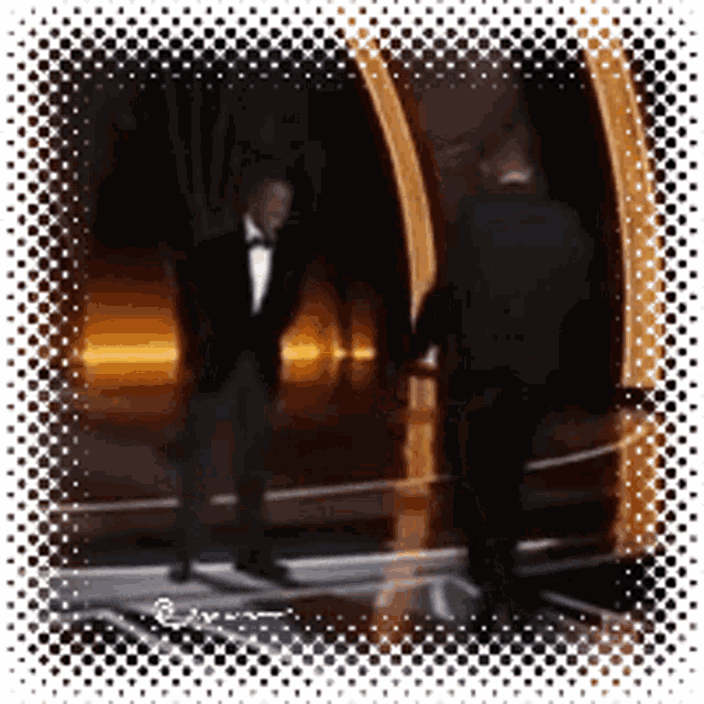 a man in a tuxedo talks to another man in a suit