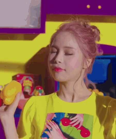 a woman with pink hair is wearing a yellow shirt and holding a yellow toy .