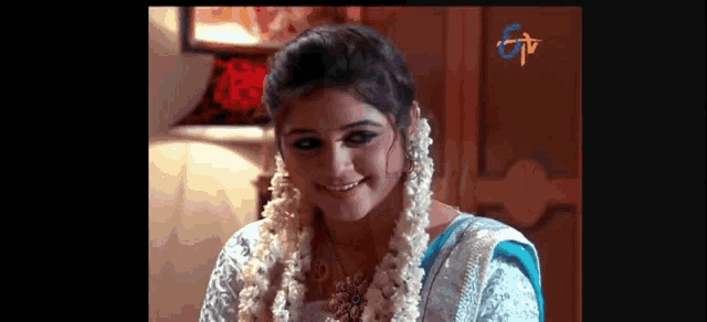 a woman in a blue and white dress is smiling and wearing a garland of flowers around her neck .