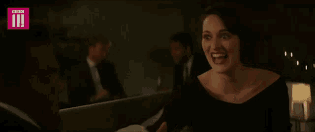 a woman in a black dress is laughing with a bbc logo behind her