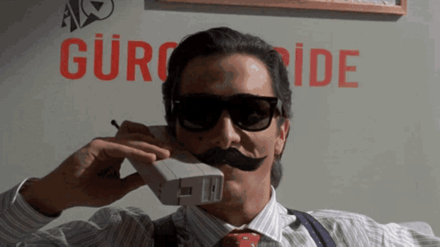 a man with a fake mustache is talking on a phone in front of a sign that says gürc ide