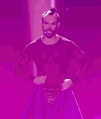 a shirtless man with a mohawk is dancing on a stage with a purple background .