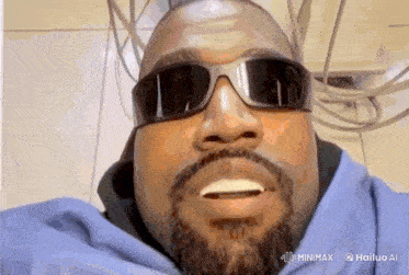 a man with a beard wearing sunglasses and a blue shirt is smiling .