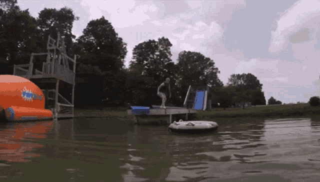 a man stands on a dock in the water near a water slide that says splash