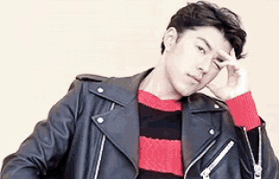 a young man wearing a leather jacket and a red and black striped sweater is holding his hand to his forehead .