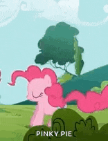 pinkie pie is standing in a field with trees in the background .